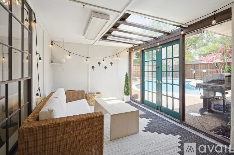 A patio with a wicker couch and a white cushion, a table, and a pool in the background.