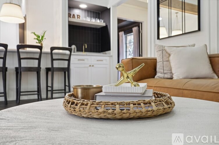A golden giraffe figurine sits on a tray with a book and a candle on a woven basket on a grey rug in a living room.