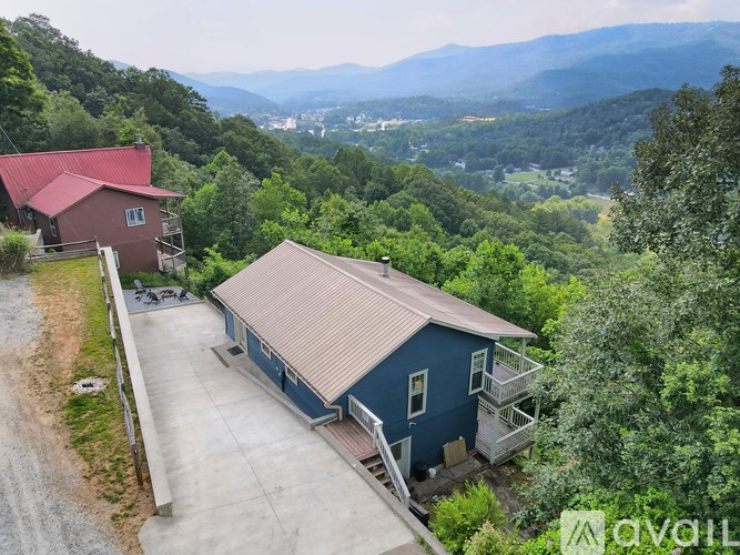 A house with a red roof is surrounded by greenery and a mountain range in the background.