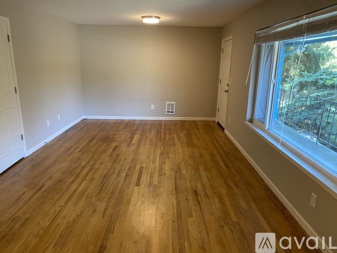 A room with wooden flooring and a window overlooking a balcony.