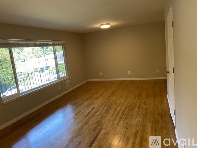 Empty room with wooden flooring and a window overlooking a balcony.