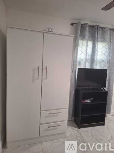 A white wardrobe with a black shelf and drawers is in a room with a window.