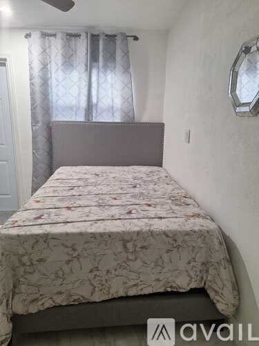 A bed with a floral patterned bedspread sits in a room with a window covered by curtains.