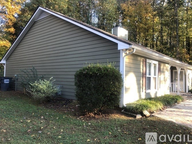 A house with a grey siding and a white trim is surrounded by greenery.