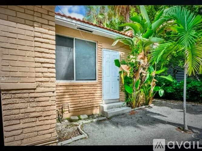 A house with a blue door and a window is surrounded by greenery.