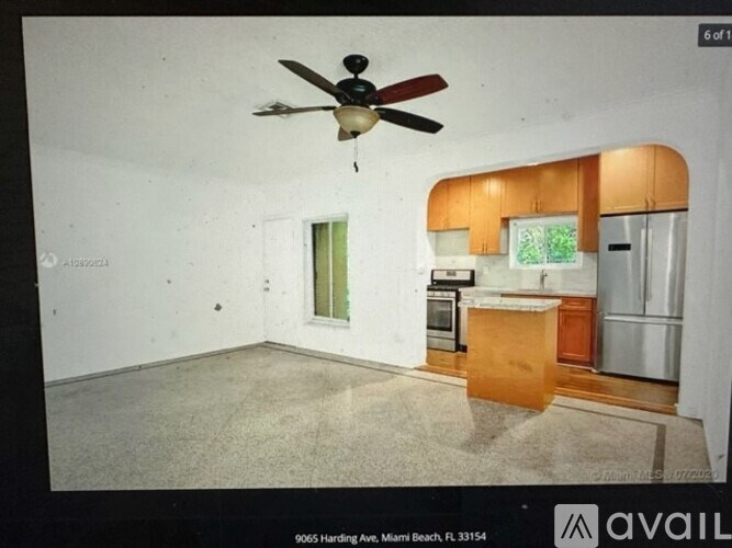 A room with a ceiling fan and a kitchenette.