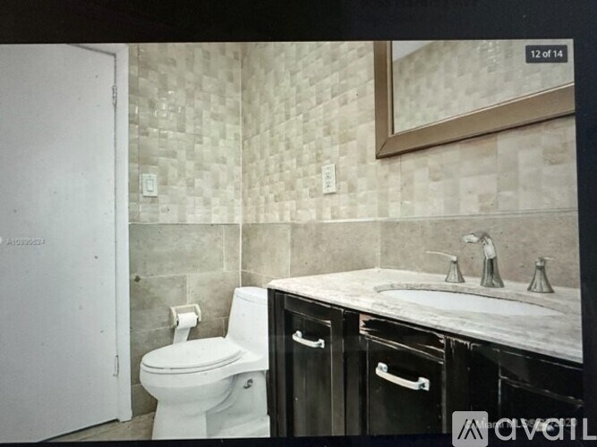 A white toilet is in a bathroom with a tiled wall and a mirror above a sink.