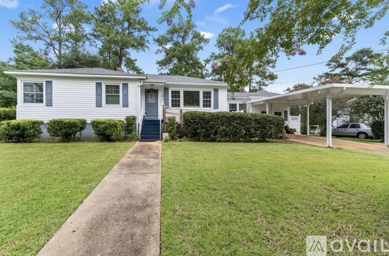 A house with a white exterior and a blue door is surrounded by greenery.