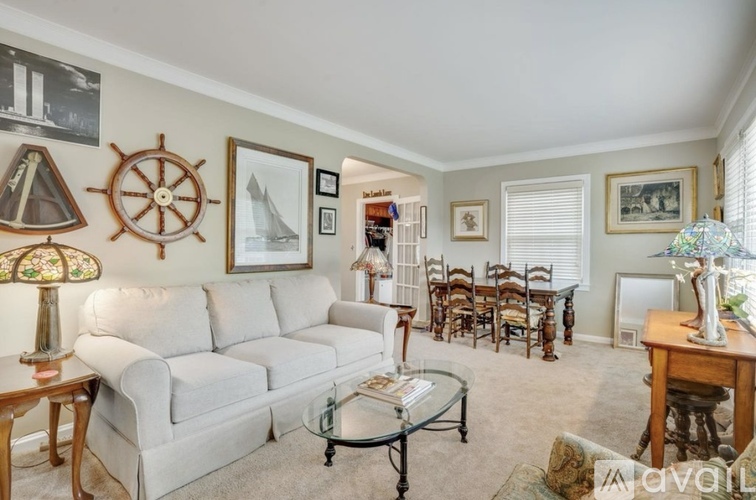 A living room with a white couch, a glass coffee table, and a ship wheel picture on the wall.