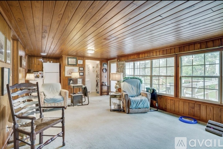 A wooden-floored living room with a blue rug and a window overlooking a deck.