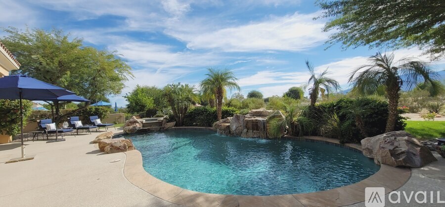 A pool surrounded by trees and rocks with a blue umbrella.