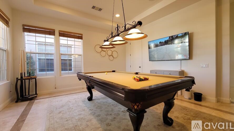 A pool table is in the middle of a room with a television mounted on the wall.