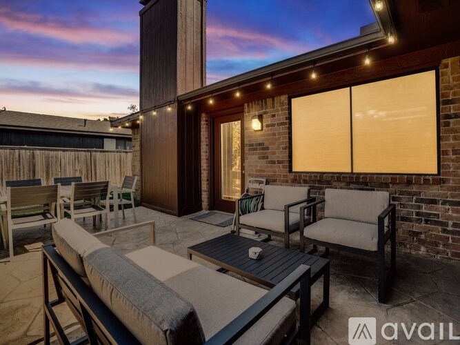 A patio with a couch, chairs, and a table is set up outside a house.