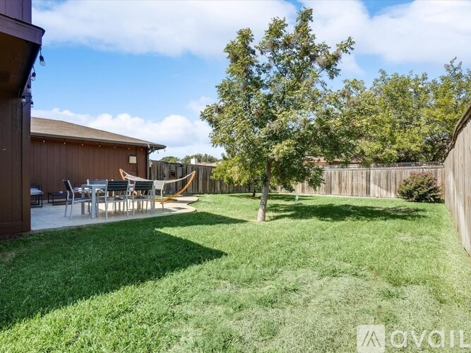 A backyard with a tree, a fence, and a patio area.