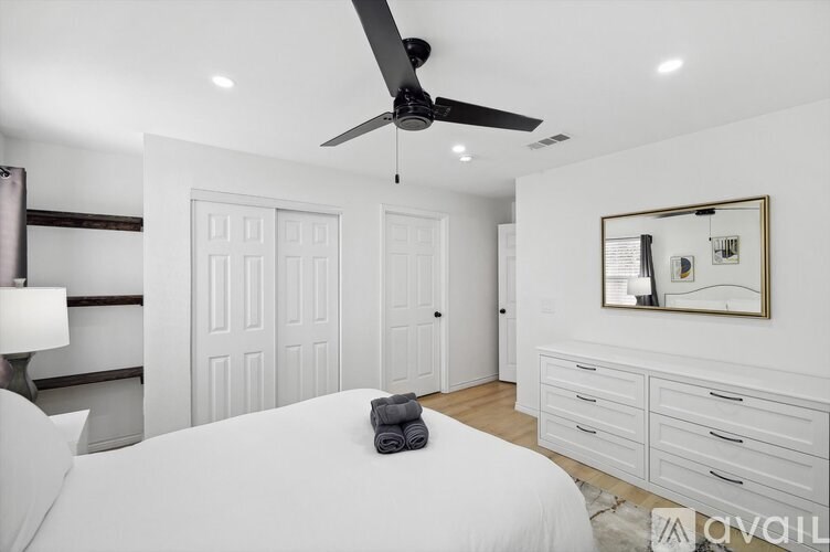 A bedroom with a white bed, a ceiling fan, and a mirror on the wall.