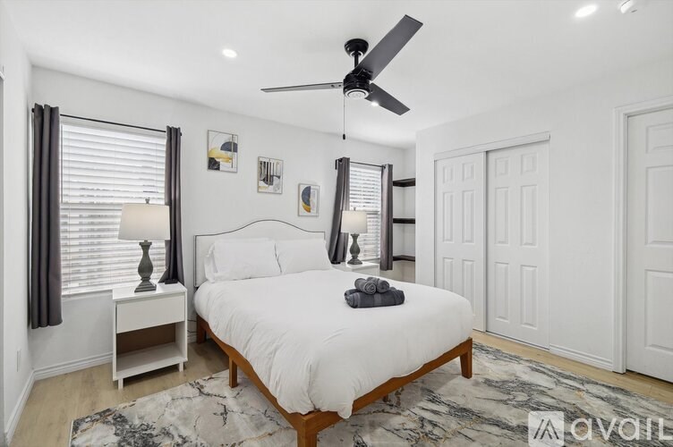 A bedroom with a white bed, a ceiling fan, and a rug on the floor.