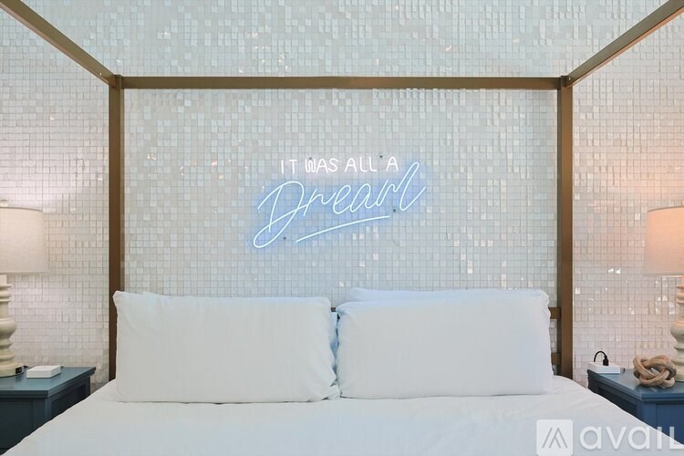 A bedroom with a bed, two lamps, and a wall with a neon sign that says "It was all a dream.".