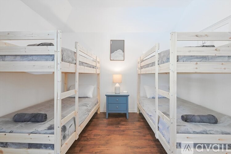A room with white walls and wooden floors has two bunk beds and a small table with a lamp on it.