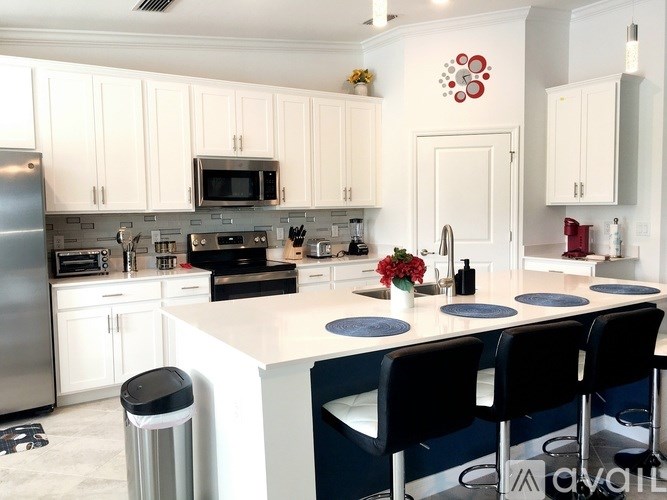 A kitchen with white cabinets and a white island with blue chairs.
