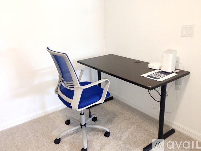 A blue and white chair is in front of a black desk with a laptop and a white cup on it.