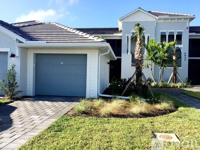 A white house with a grey garage door and a palm tree in front.