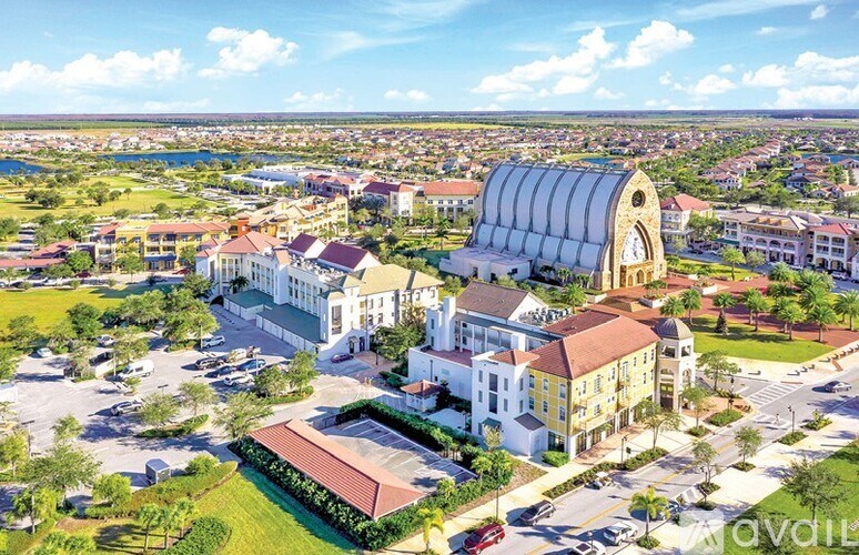 A large white building with a red roof is surrounded by smaller buildings and greenery.