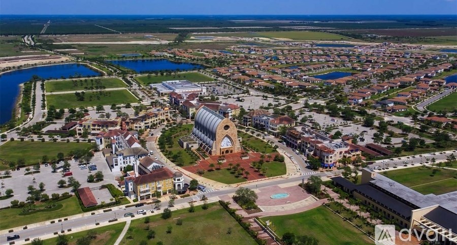 An aerial view of a town with a large building in the center and a body of water to the left.