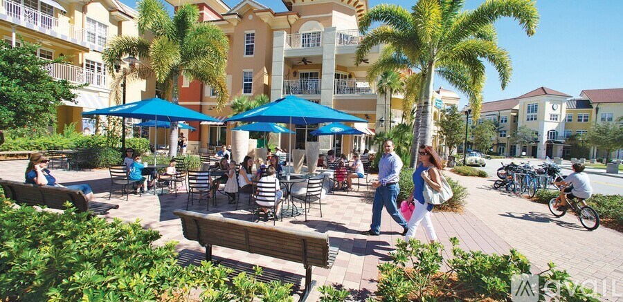A group of people are sitting at tables under blue umbrellas in a courtyard.