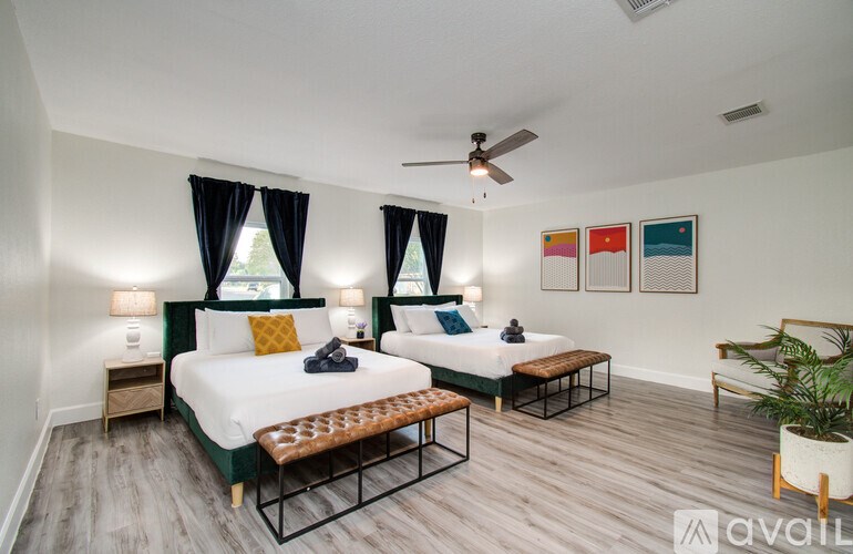 A bedroom with two beds, each with a white bedspread and a yellow pillow, a ceiling fan, and a potted plant.