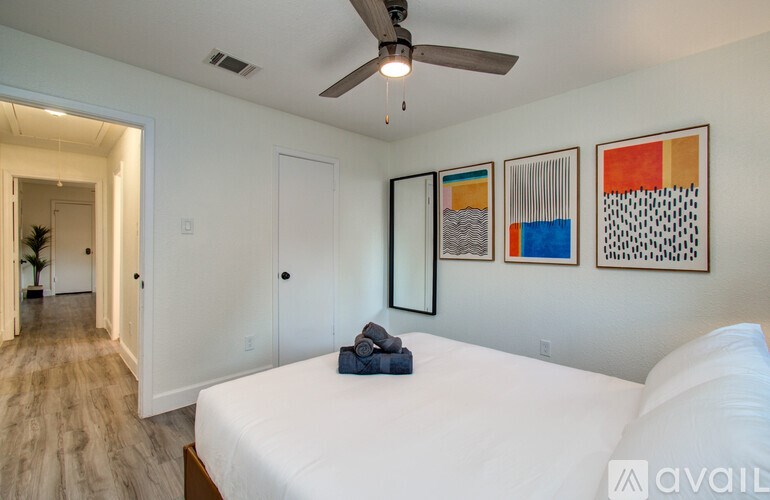 A bedroom with a bed, a ceiling fan, and three framed artworks on the wall.