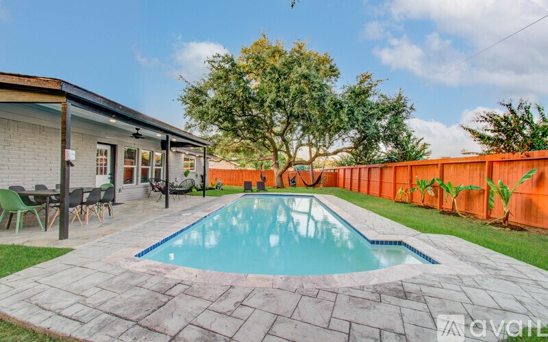 A pool surrounded by a stone patio and a wooden fence.