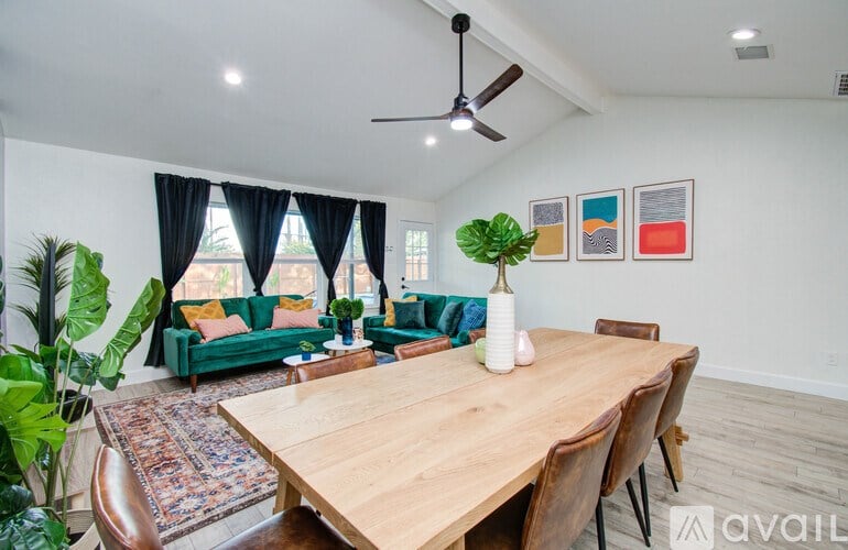 A room with a wooden table and chairs, a ceiling fan, and a couch with a green cushion.