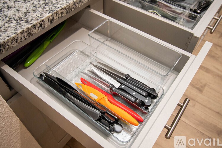 A drawer with a clear plastic divider contains a set of knives.