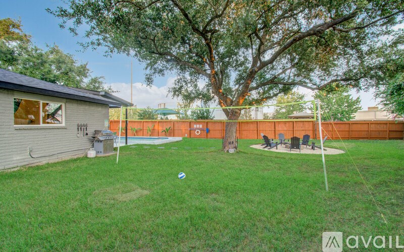 A backyard with a tree, a fence, and a ball on the grass.