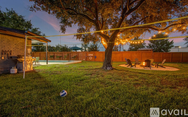 A backyard with a tree, a fire pit, and a building with a sign that says "available".