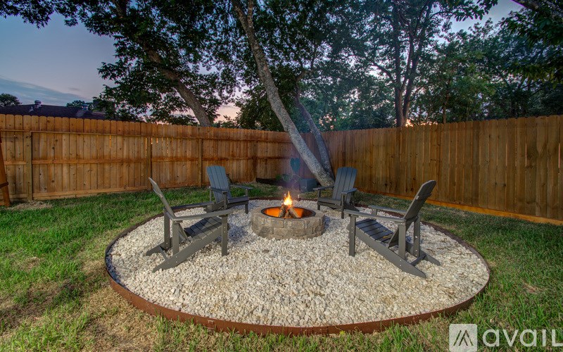 A fire pit in a backyard surrounded by chairs and a fence.