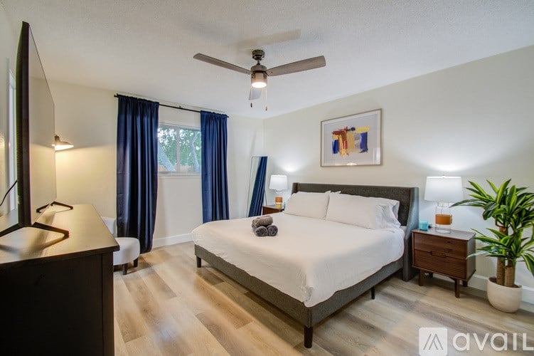 A bedroom with a large bed, a ceiling fan, and a painting on the wall.