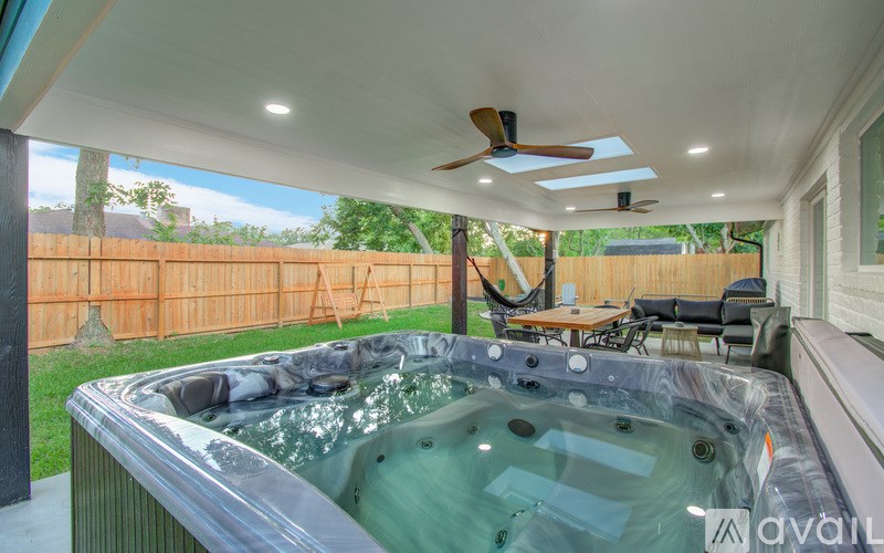 A hot tub is in the middle of a patio with a ceiling fan and a deck.
