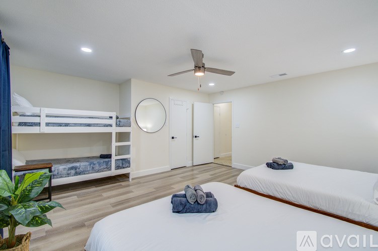 A bedroom with a white bed, a ceiling fan, and a bunk bed with a blue blanket.