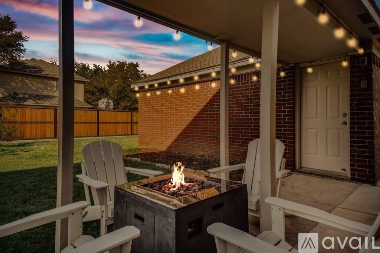 A patio with a fire pit and chairs under string lights.
