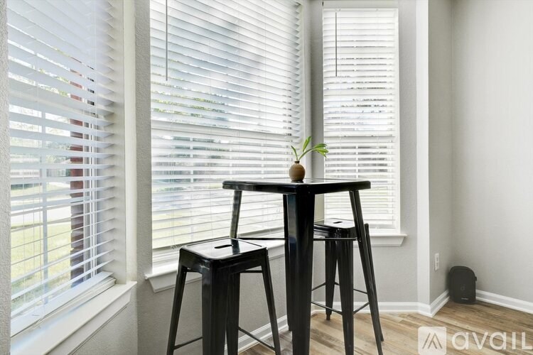 A small table with a plant on it sits in front of a window with blinds.