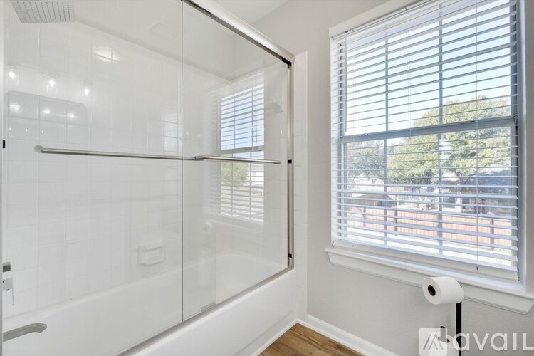 A bathroom with a glass shower stall and a window with blinds.