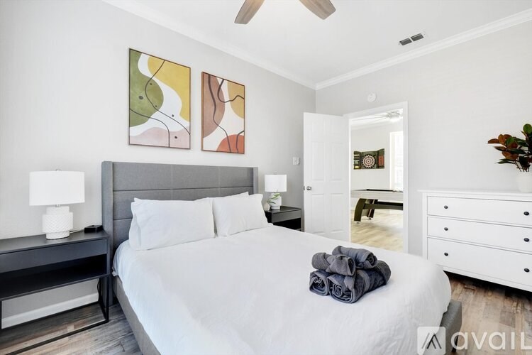 A bedroom with a large bed, a ceiling fan, and a painting on the wall.