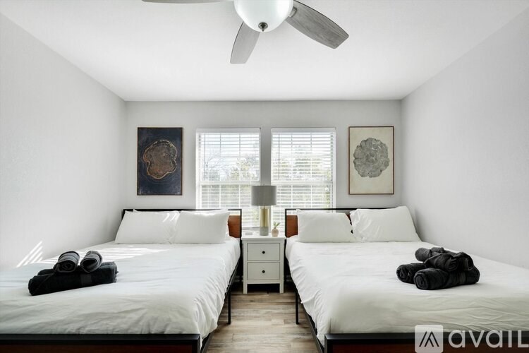 A bedroom with two beds, a ceiling fan, and two wall art pieces.
