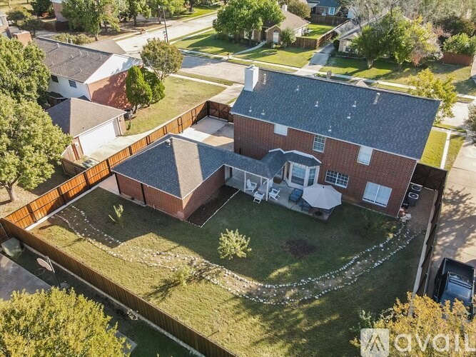 A house with a red brick exterior and a white garage door is surrounded by a grassy yard.
