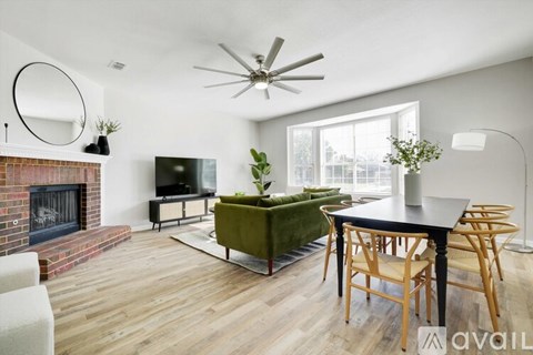 A living room with a fireplace, a green sofa, a wooden dining table and chairs, and a ceiling fan.