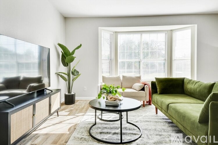 A living room with a green couch, a black coffee table, and a large window with blinds.