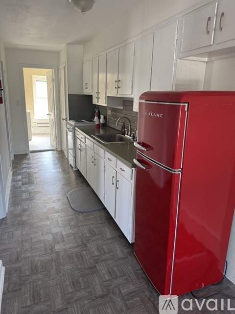 A red refrigerator is in the middle of a kitchen with white cabinets.