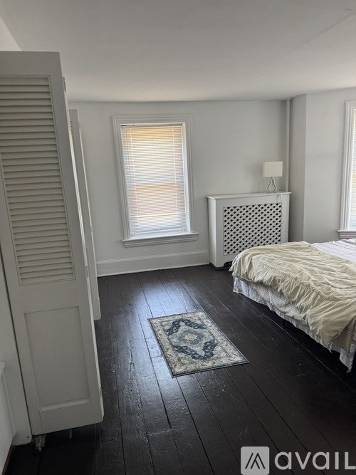 A bedroom with a bed, a window with blinds, and a radiator on the wall.