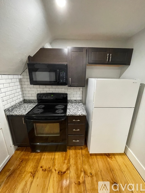 A kitchen with a black oven and microwave, a white fridge, and wooden floors.